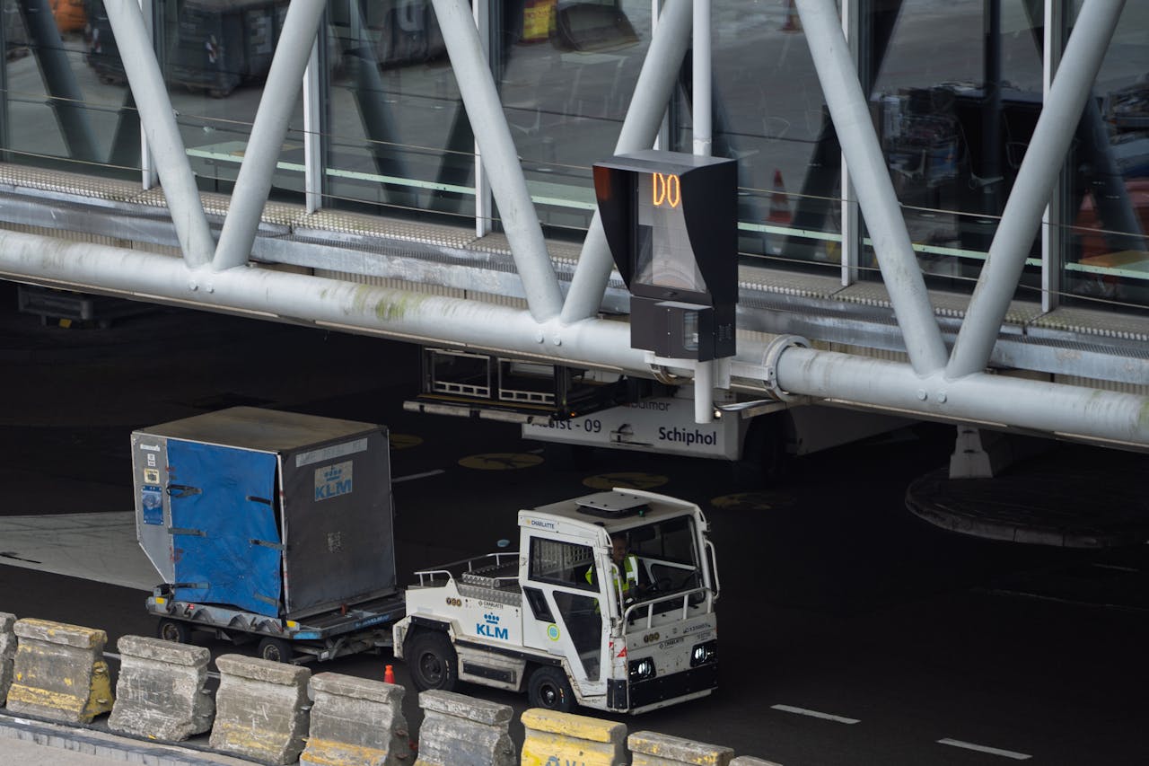 KLM ground services vehicle and cargo near Schiphol airport terminal bridge.