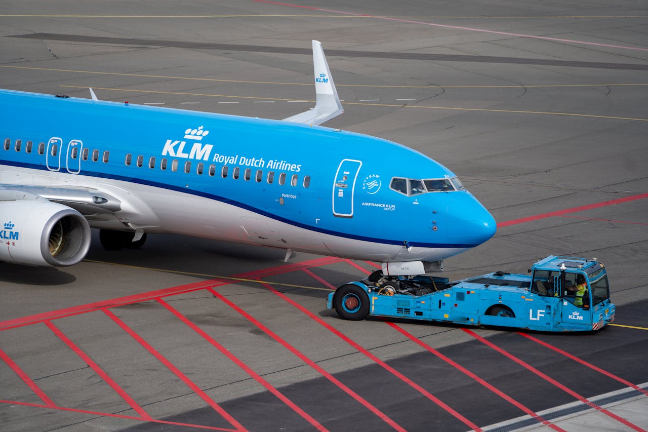 KLM aircraft on tarmac being towed by a blue tug vehicle at the airport.
